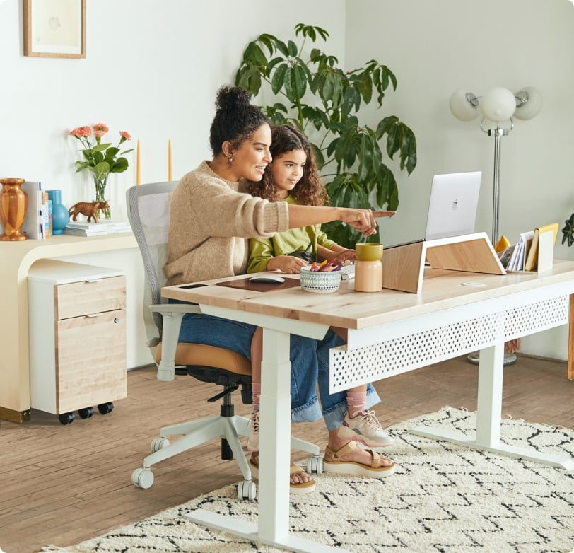 Mother and daughter looking at a computer together. The mother is wearing a beige sweater and pointing at refinance information.
