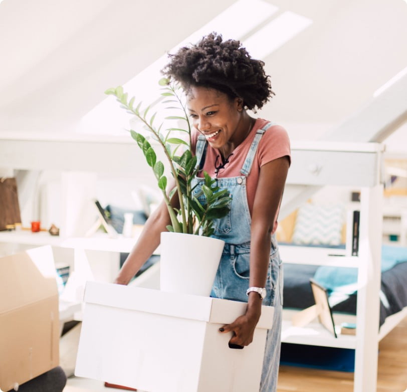 Woman preparing for home buying by moving a white box with a plant on top