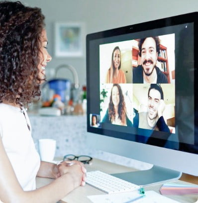 Woman looking at a computer screen that shows a remote meeting taking place. Everyone is smiling.